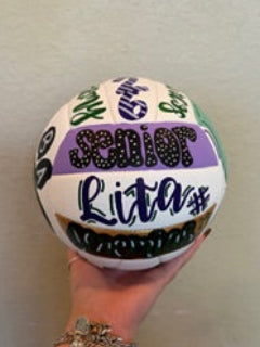 Hand holding a colorful volleyball against a plain background